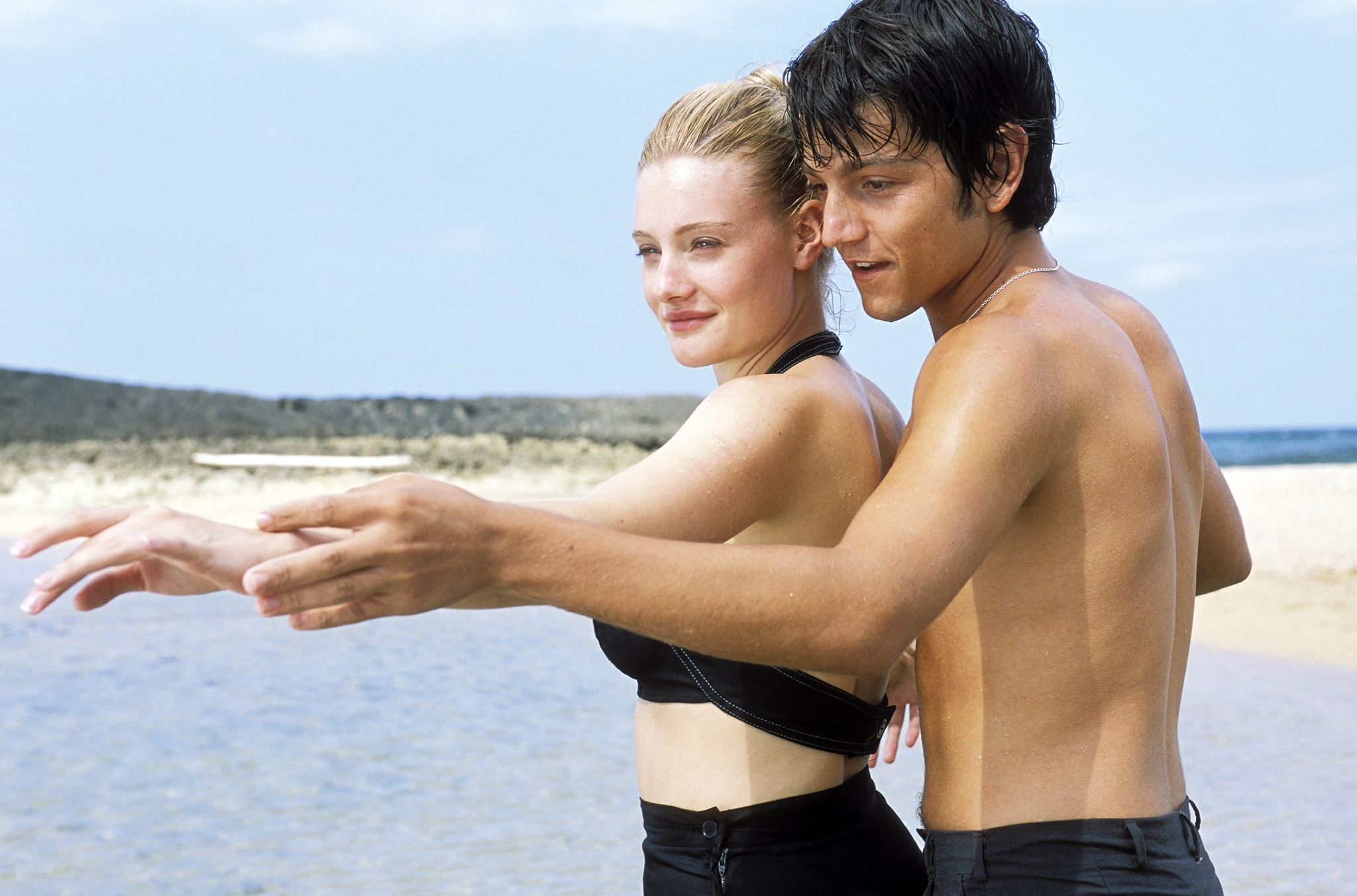 scene from dirty dancing havana nights where diego luna - shirtless with black shorts - teaches romola garai (wearing a black two piece swimsuit) some moves beside a beach