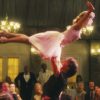 scene from climax of 1987 film dirty dancing where patrick swayze as johnny - wearing black shirt and pants - stands amidst the audience and lifts jennifer grey as baby - wearing a pink dress with flowing skirt and tight bodice - over his head
